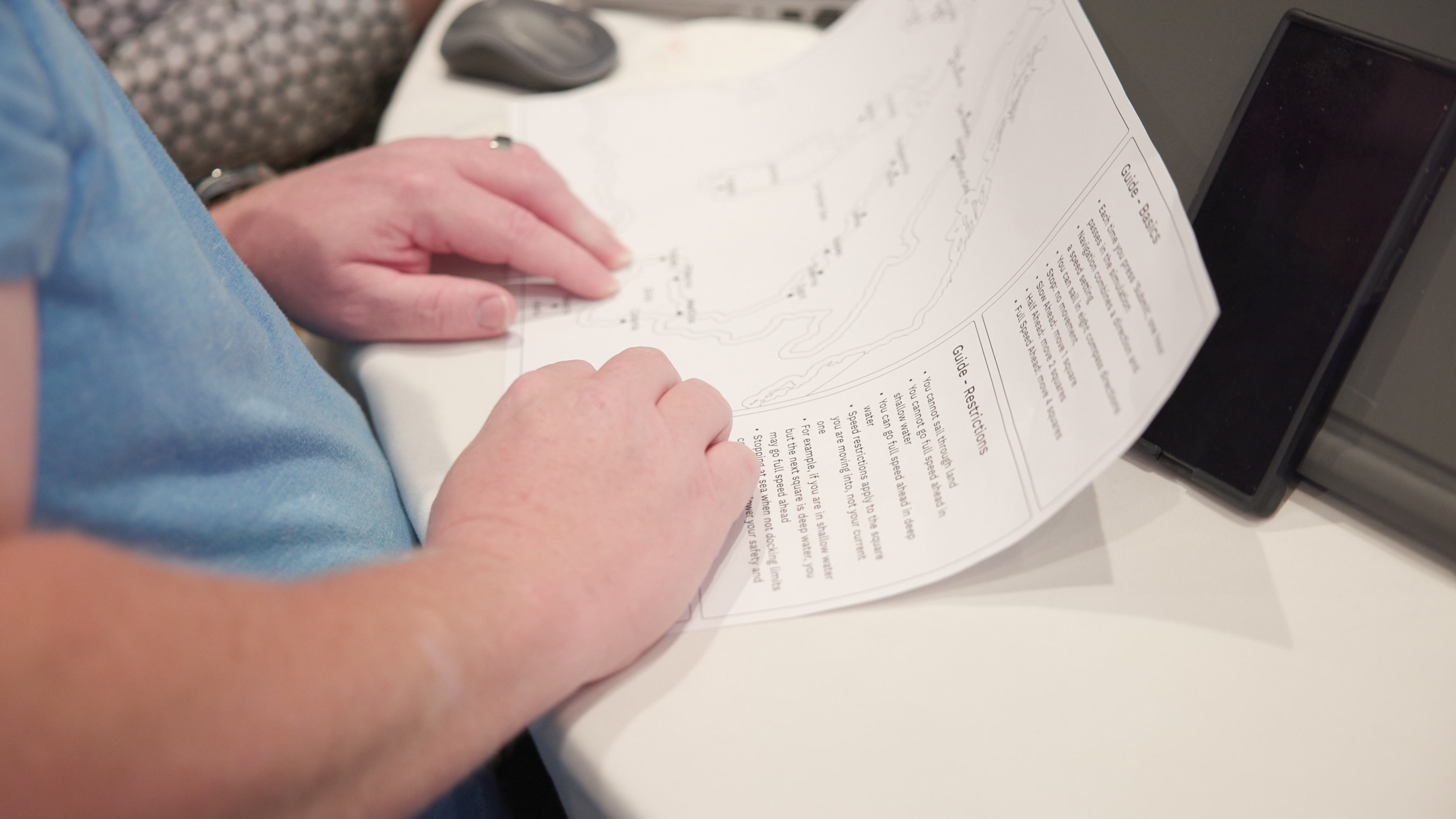 A close-up over the shoulder of a person holding and reading a printed guide with simulation rules.