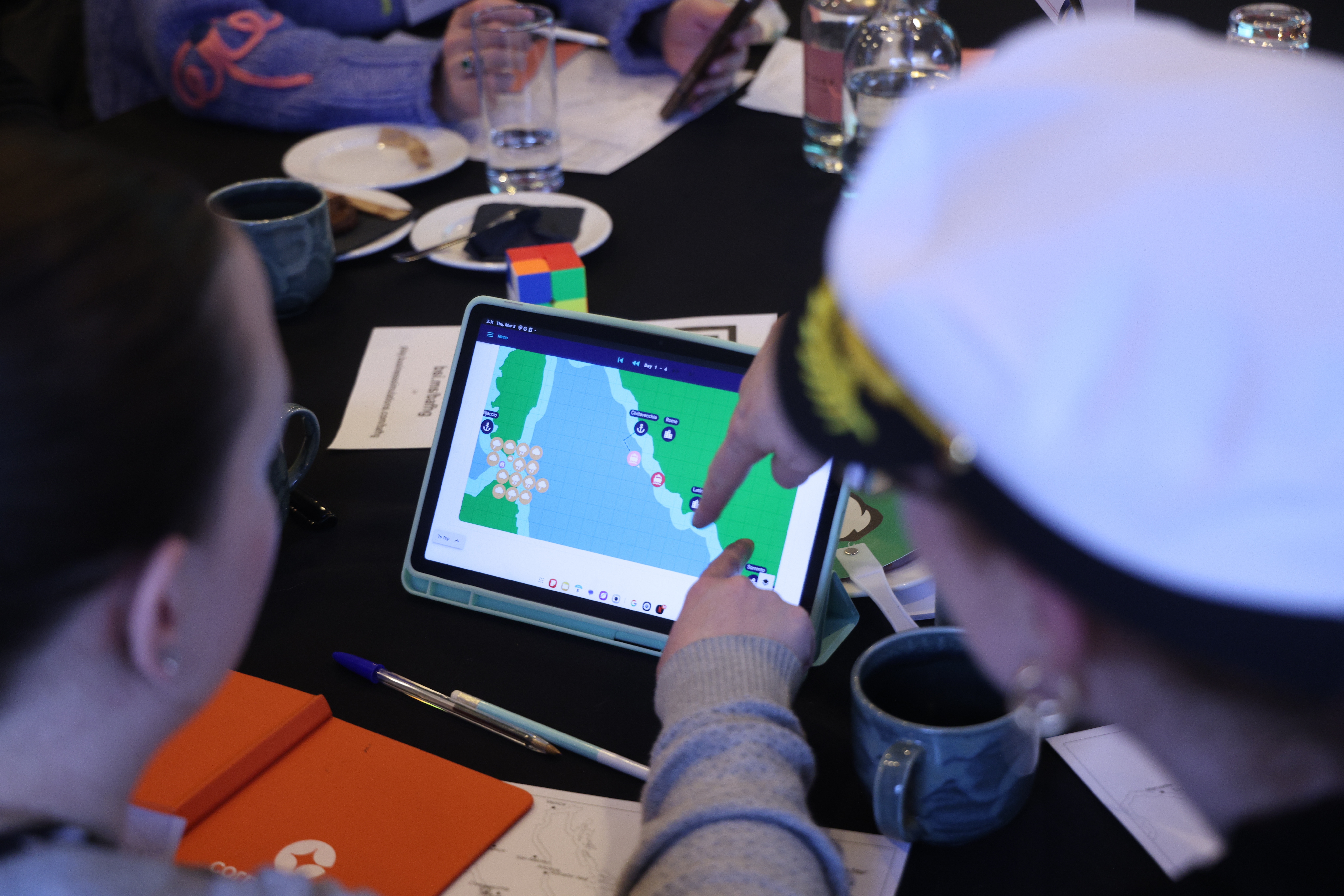 Team members view a strategic business simulation map on a tablet during a facilitated business game session.
