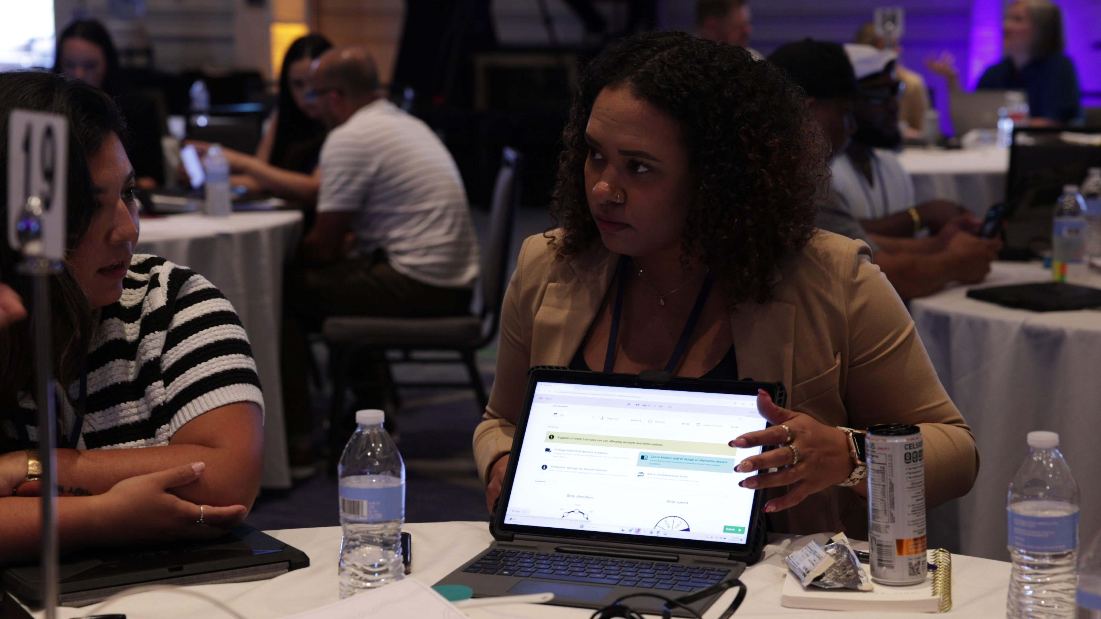 Two women sit at a round table in a conference room, discussing information displayed on a tablet screen.