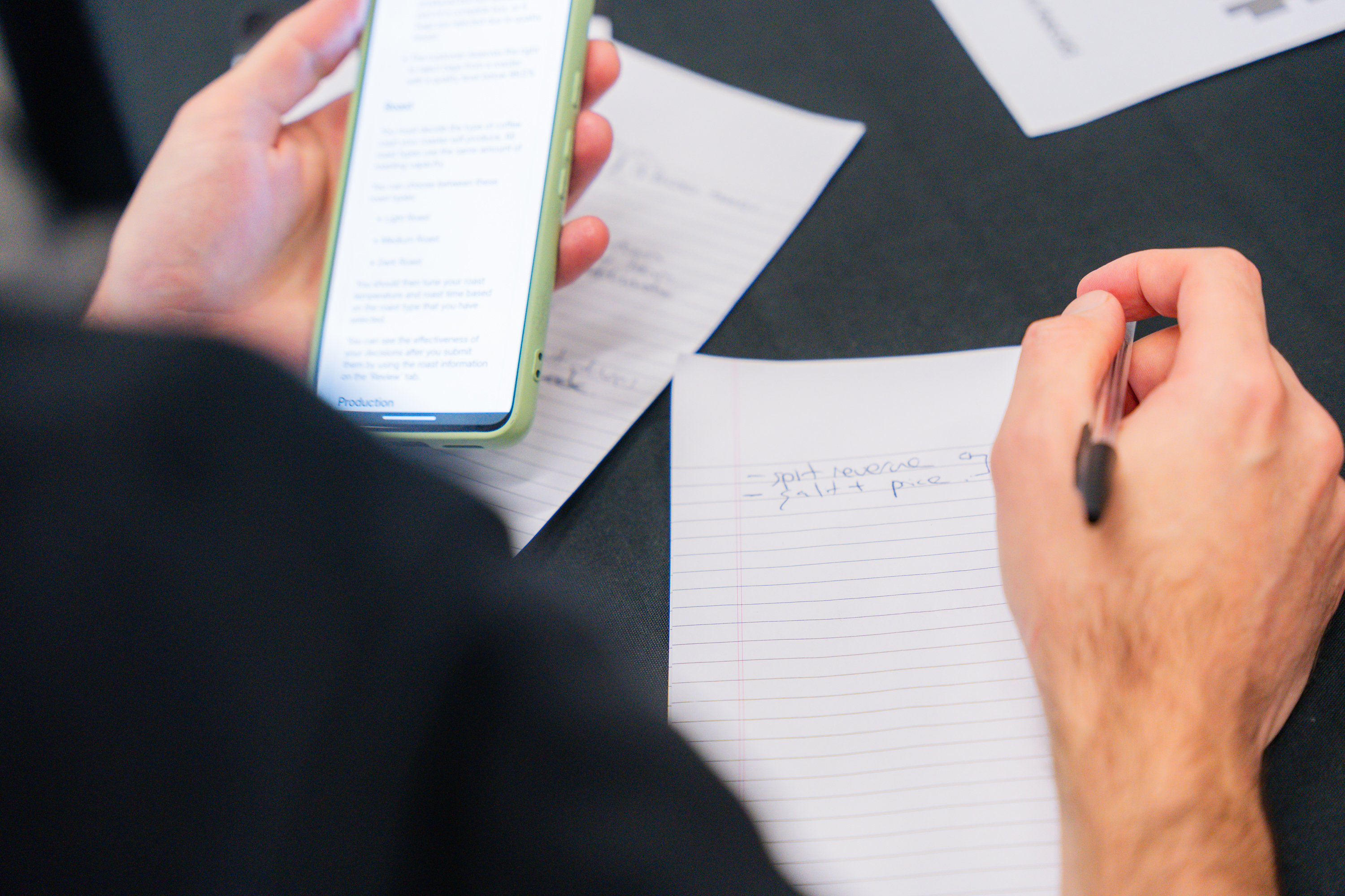 Team members reviewing documents and mobile phone during business simulation meeting at table