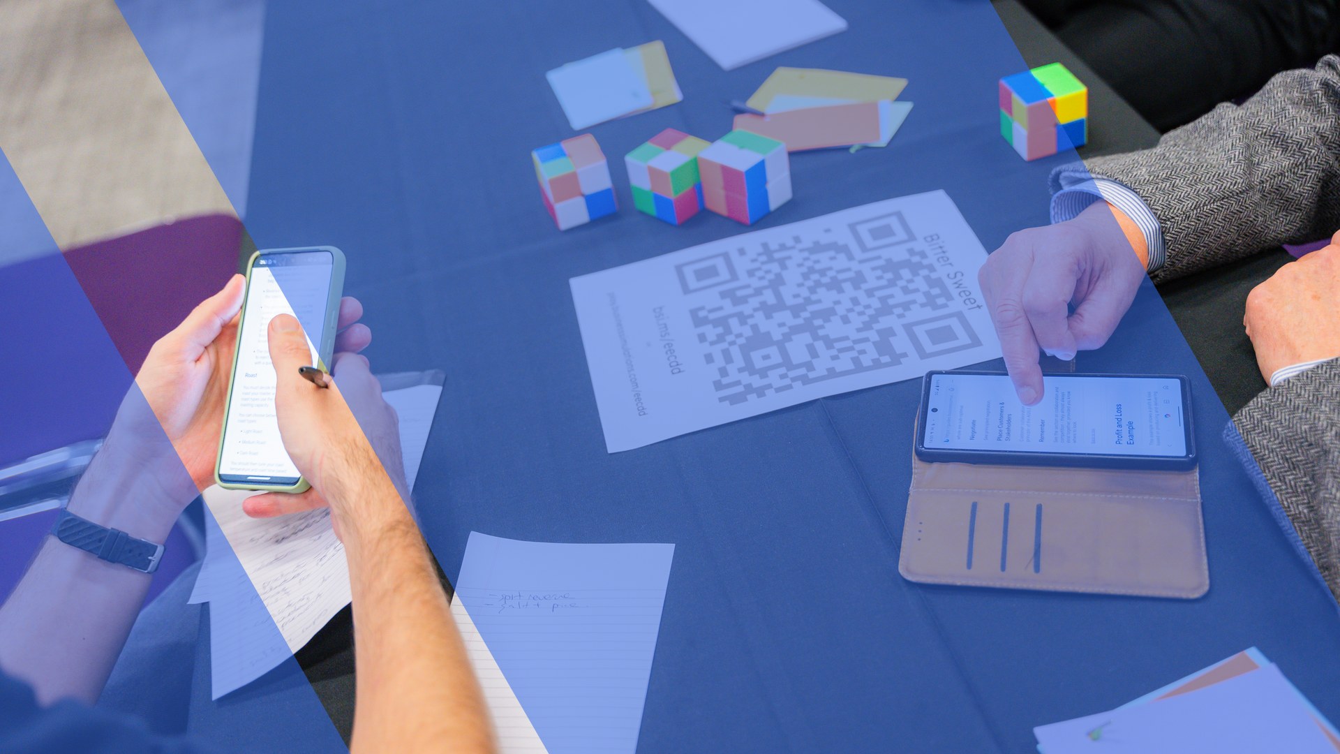 Participants use the simulation platform on their phones during an innovation-themed business simulation, with puzzle cubes and notes on the table, overlaid with the Business Simulations brand motif