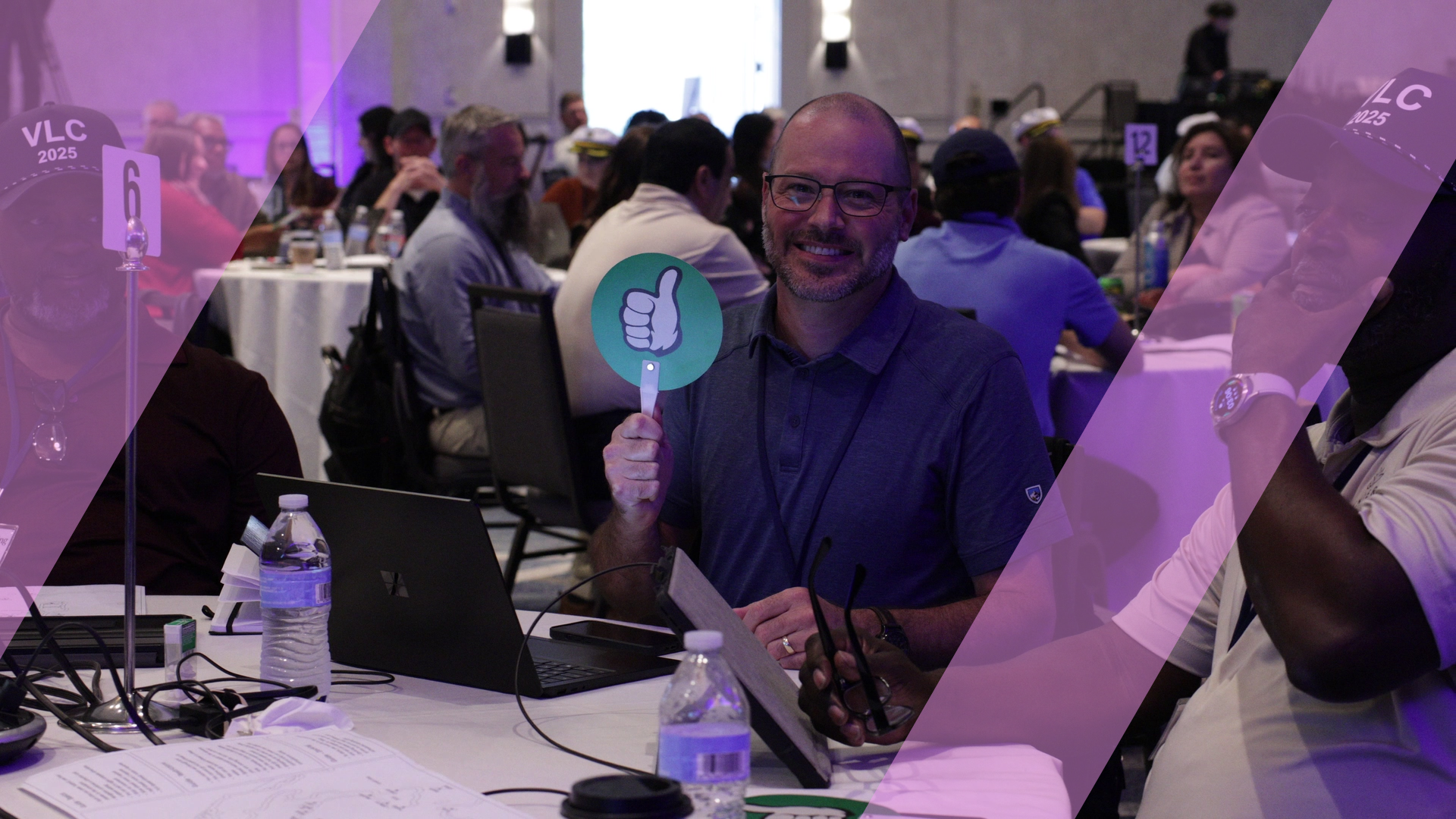 A participant holding up a green thumbs-up paddle and smiling during a business simulation.