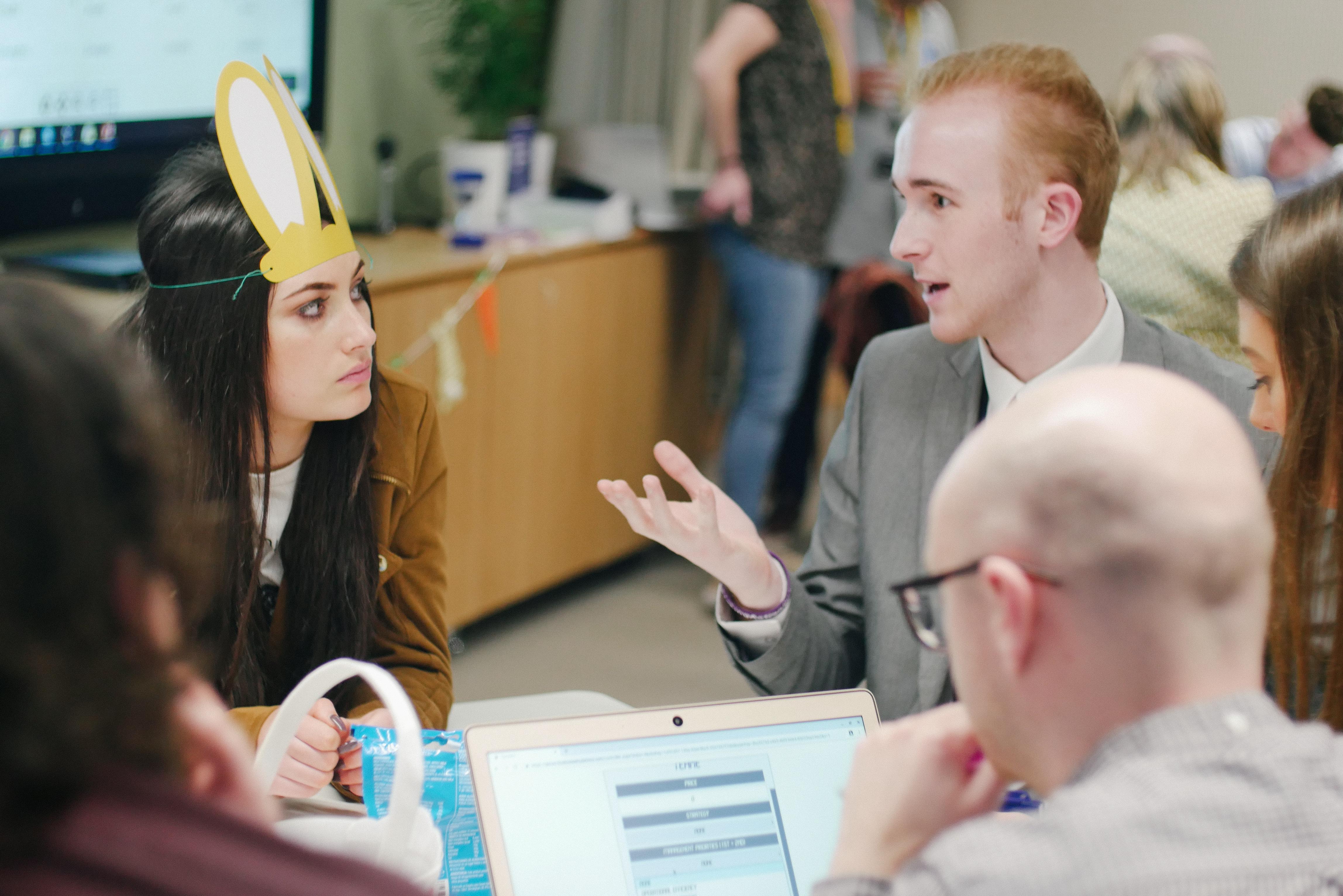 Two colleagues in an open, honest conversation during a team business simulation, one explaining while the other listens