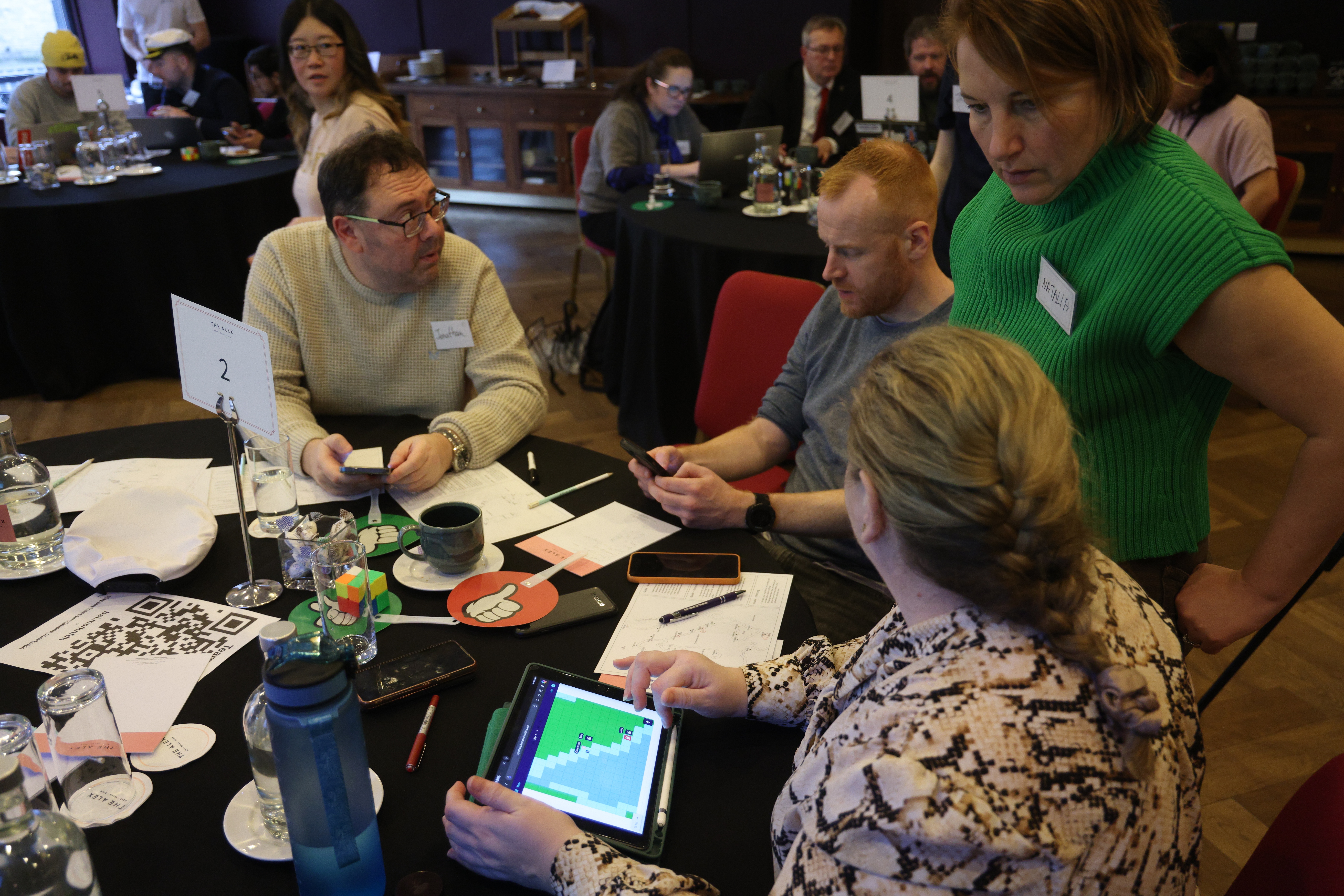 Business simulation participants reviewing performance data on a tablet and discussing the numbers as a team