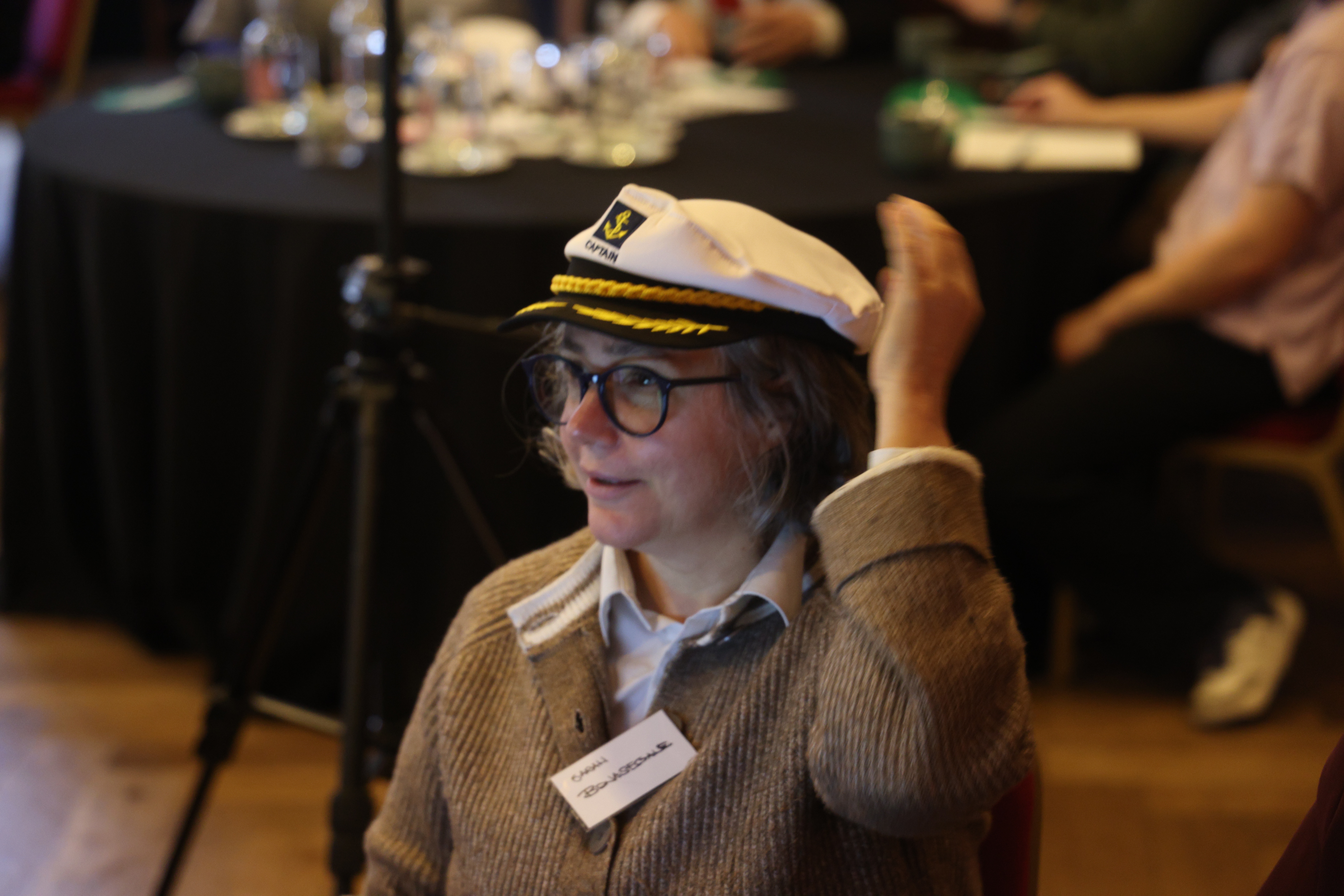 Participant wearing captain's hat and glasses at a Business Simulations facilitated event, smiling at team gathering.