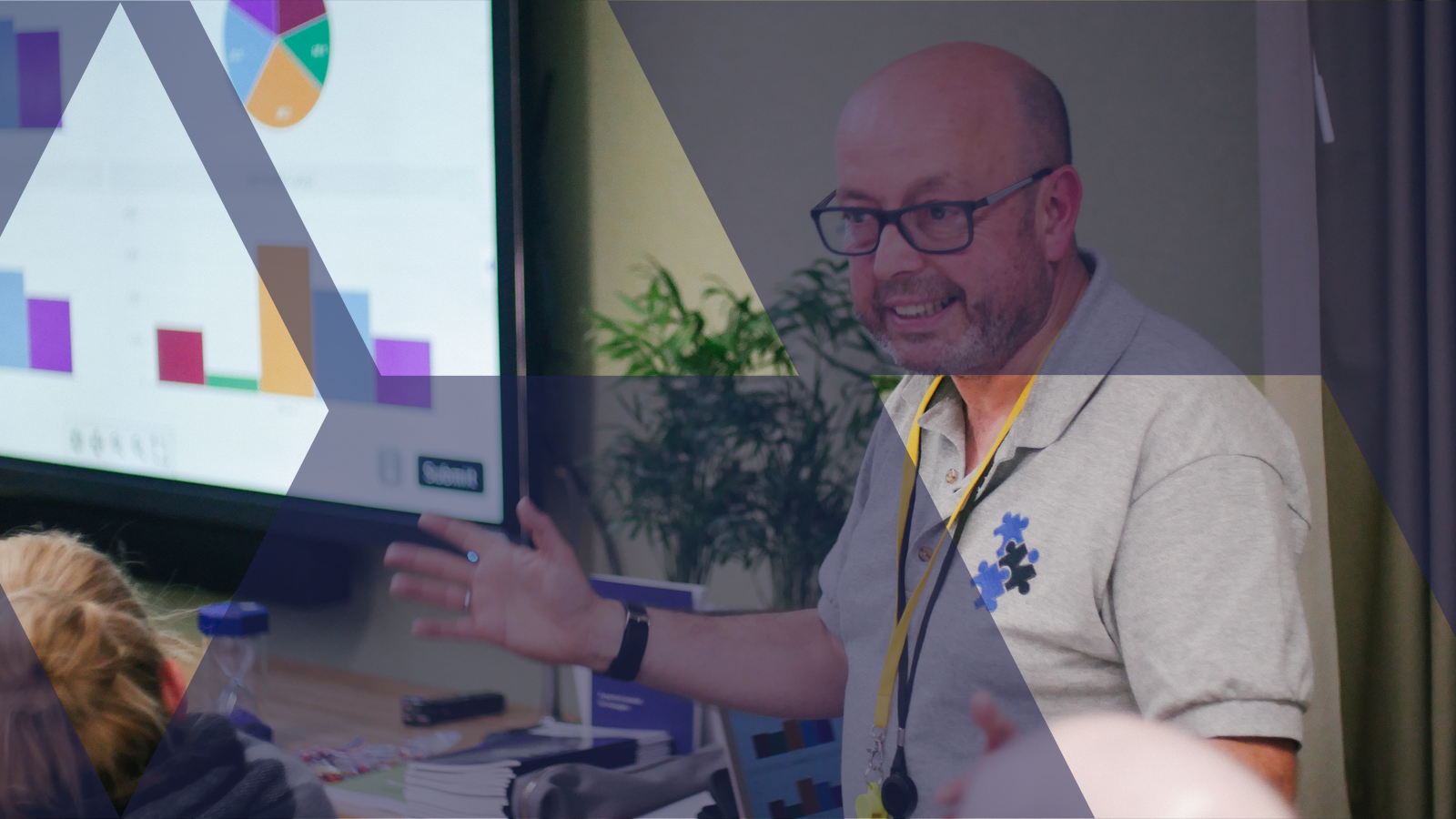 A facilitator engaging a team beside a live data dashboard during a business simulation, with the Business Simulations brand motif overlaid in deep navy