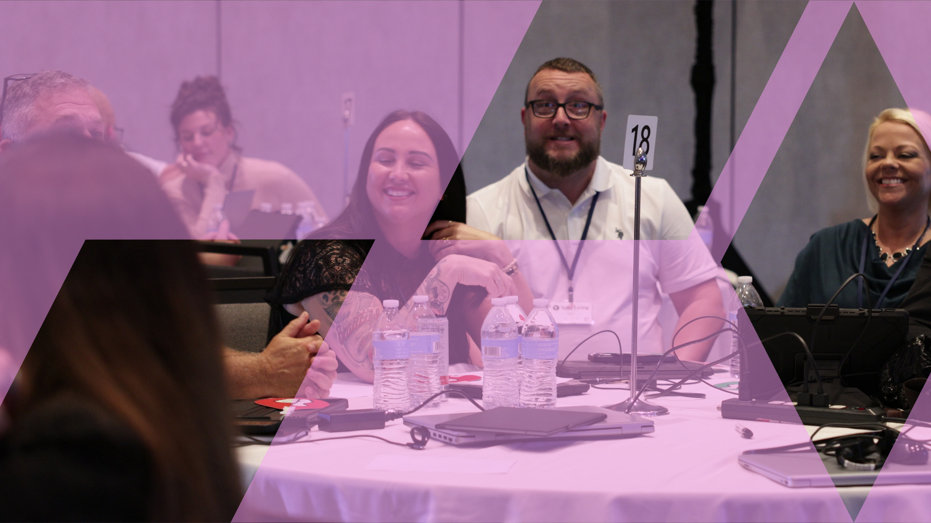 Two participants smiling broadly at their table during a business simulation, laptops and materials in front of them.