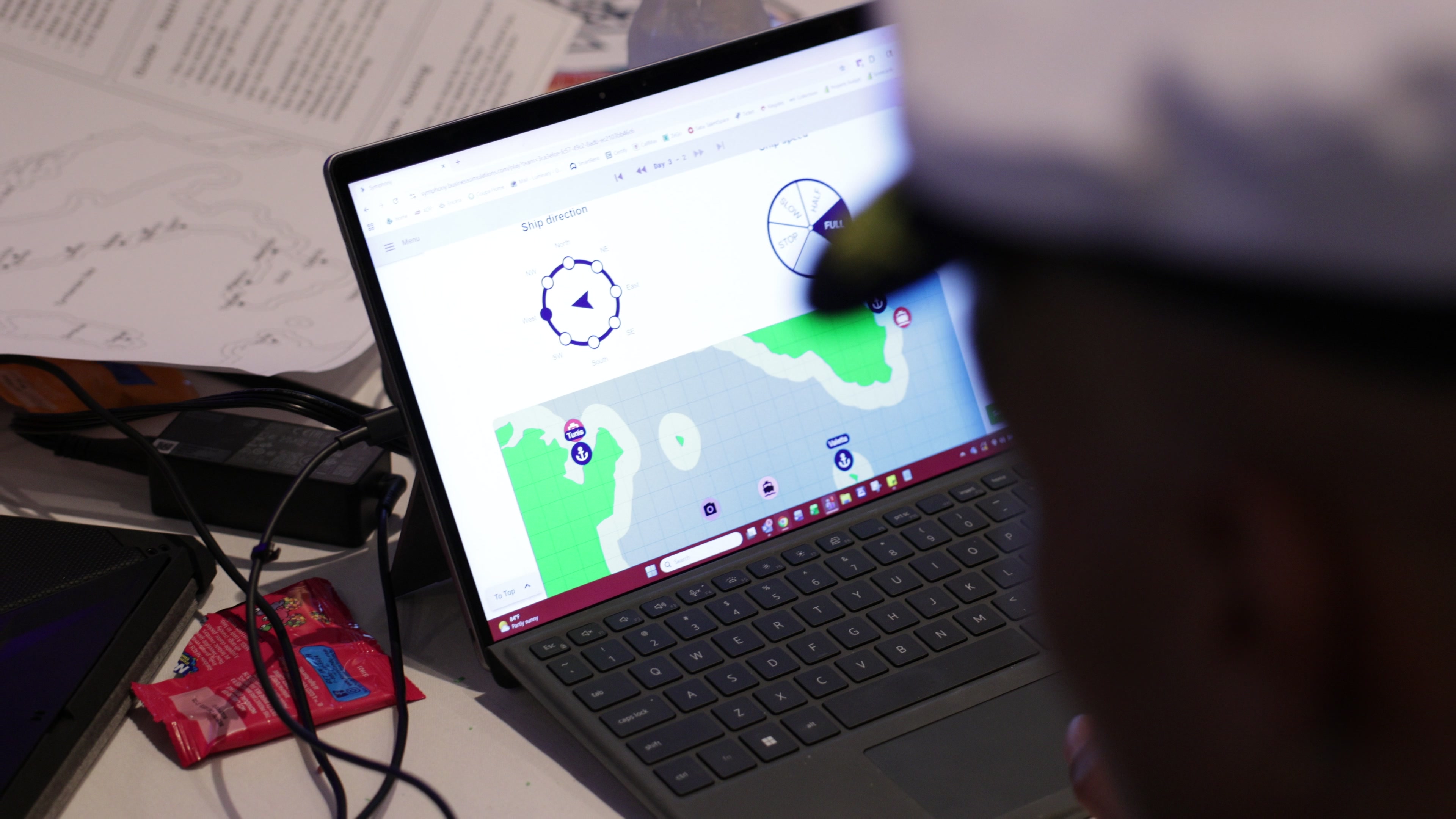 Over-the-shoulder view past a person wearing a white captain's hat to a tablet screen showing a maritime navigation interface.
