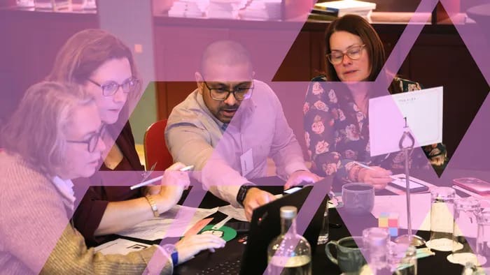 Business simulation participants reviewing performance data on a tablet and discussing the numbers as a team