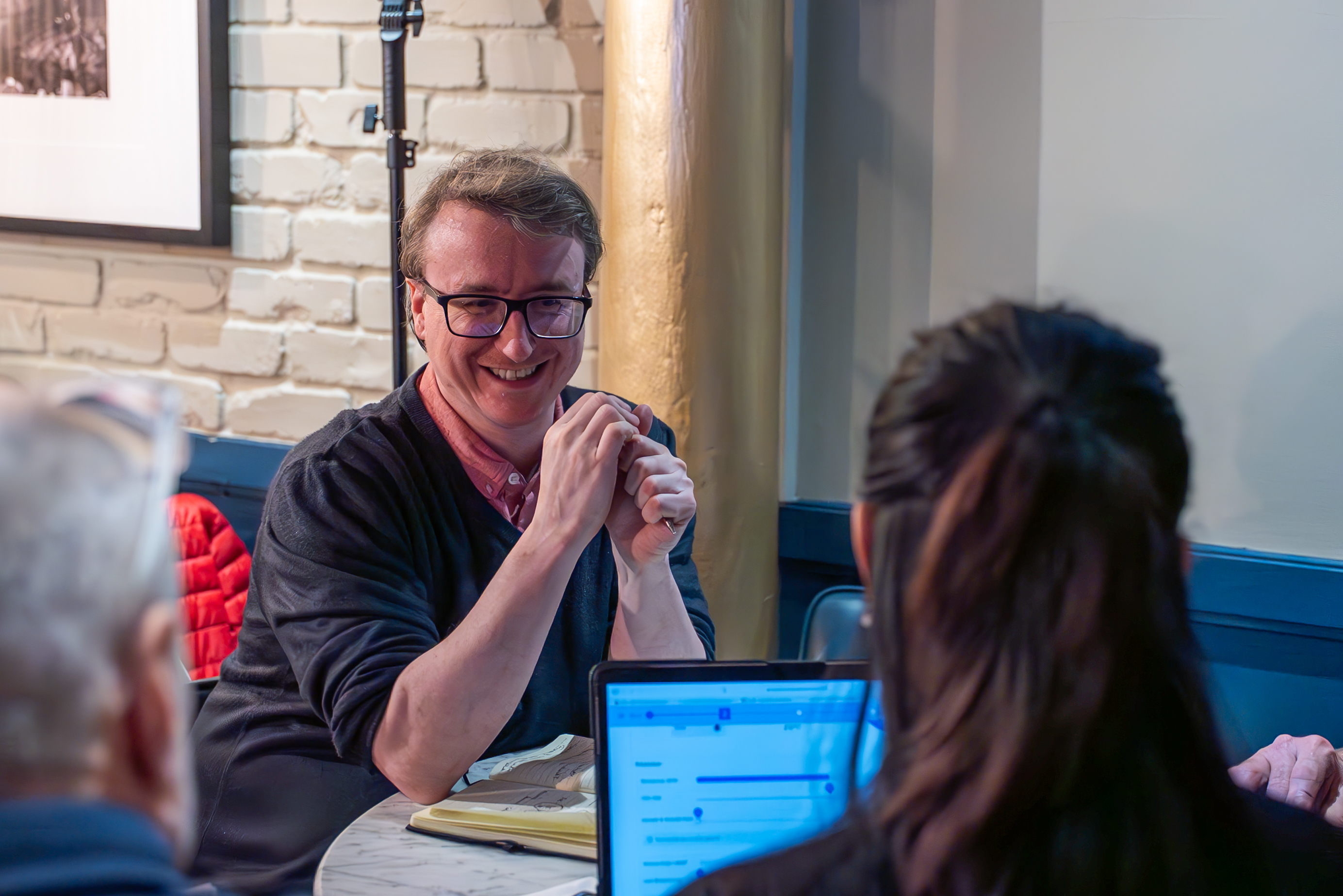 Facilitator smiling while speaking to participants during a business simulation session at a table with laptops.