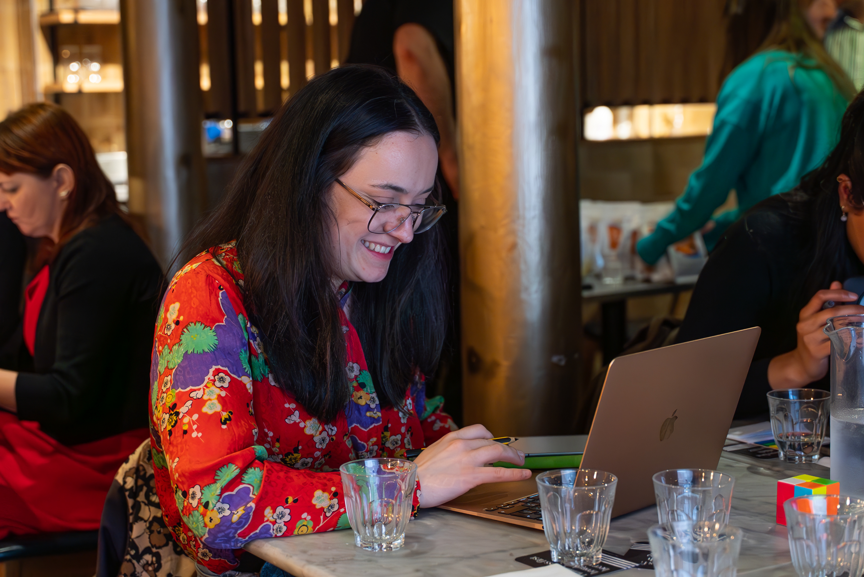 Woman wearing glasses and colorful floral jacket uses laptop during business simulation workshop