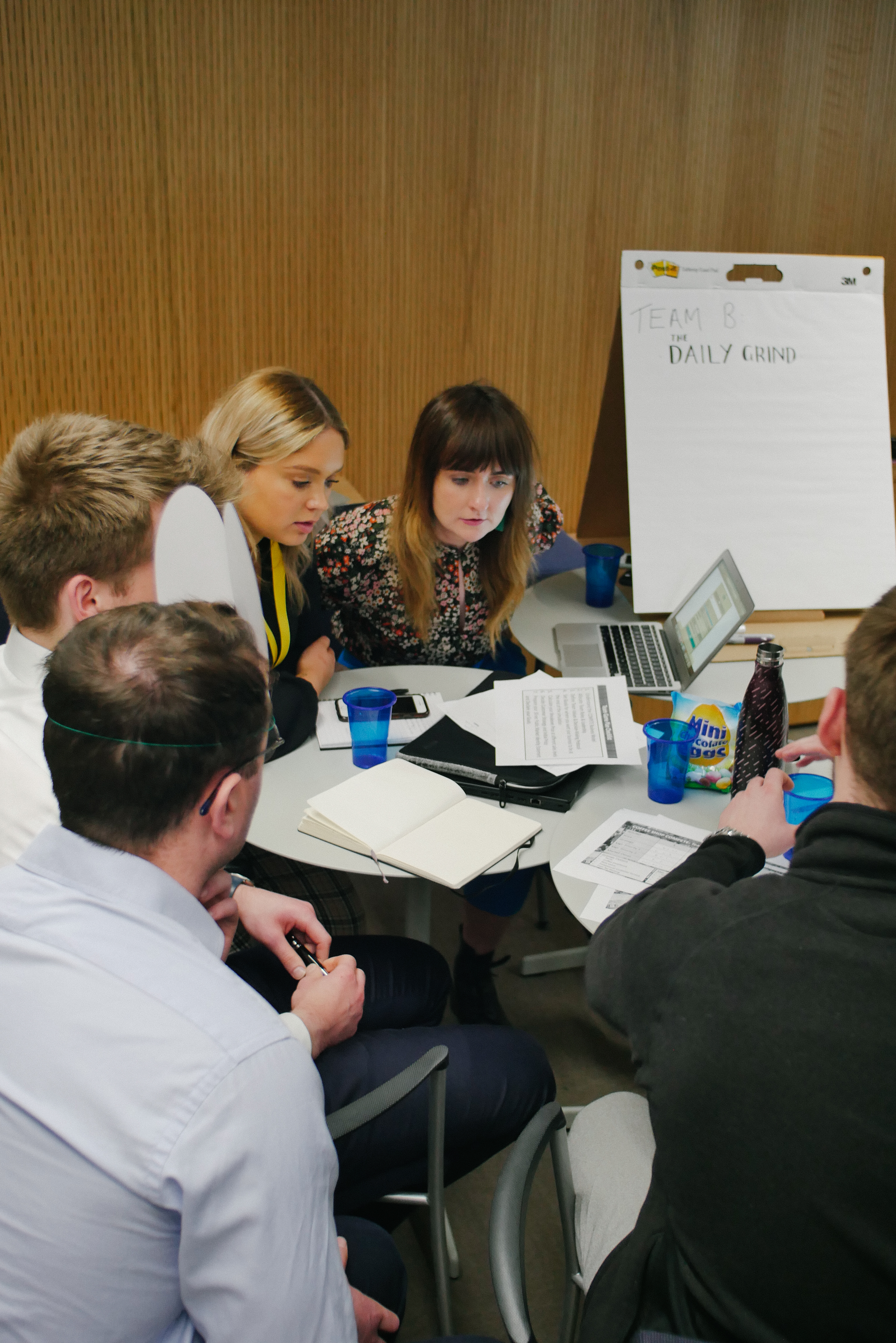 Team members engaged in discussion around a table during a business simulation workshop.