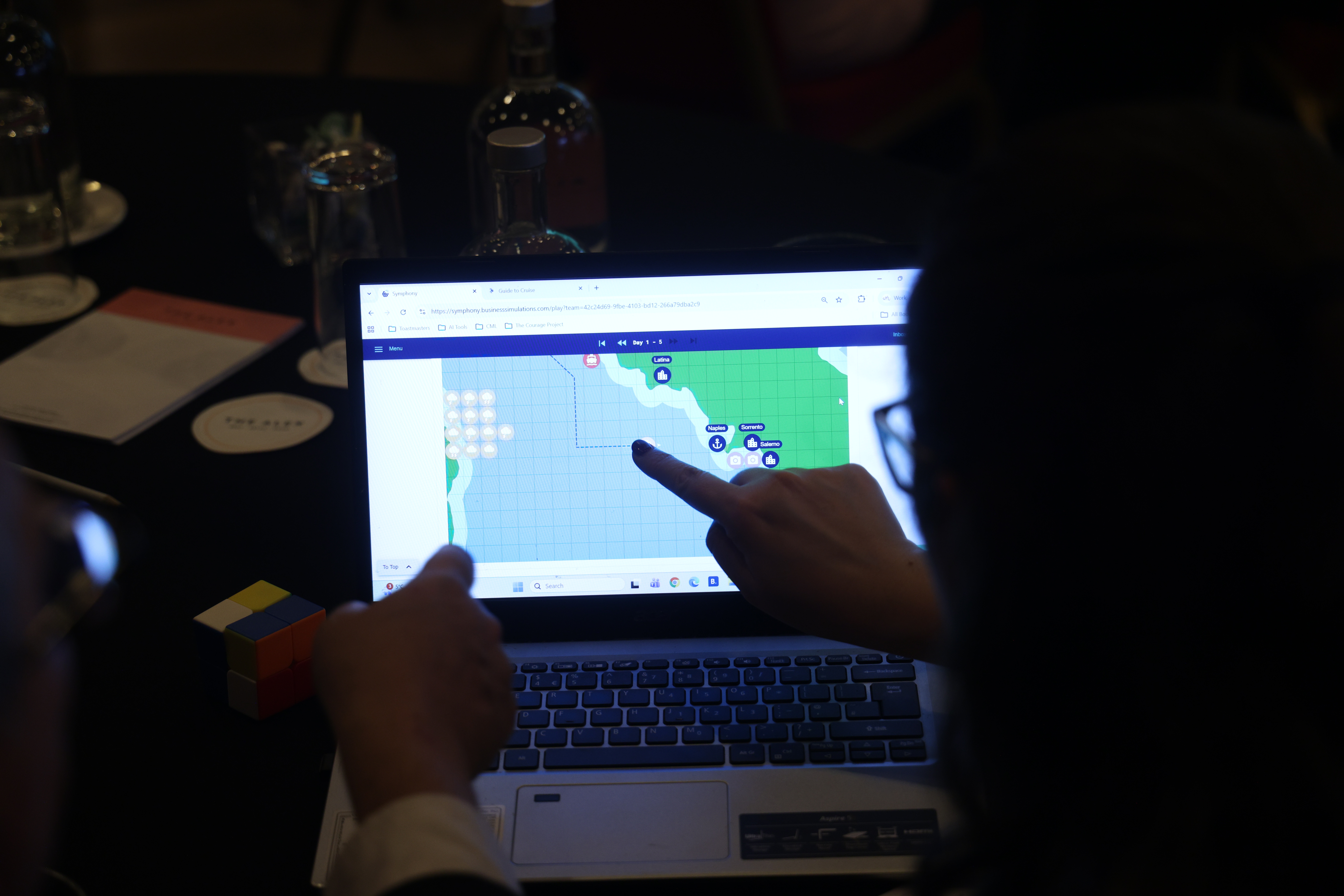 Participant points at supply chain logistics map on laptop screen during business simulation exercise