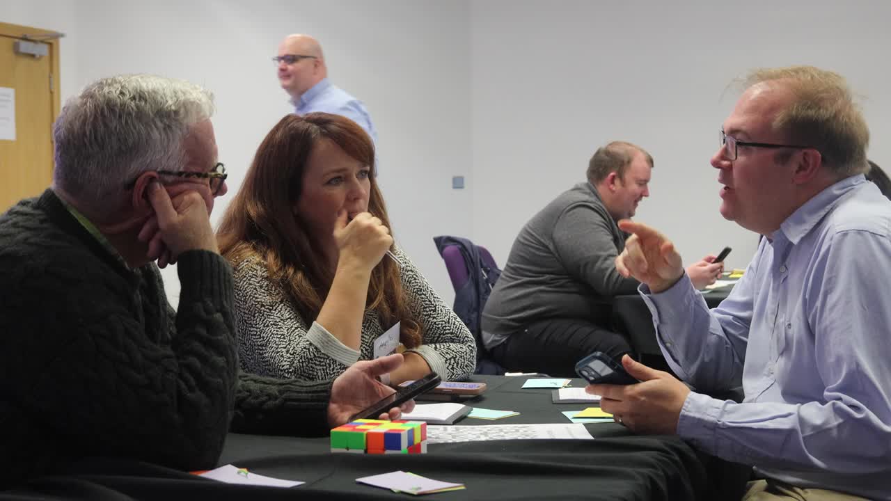 Three workshop participants in discussion at a table, one making a point while two listen